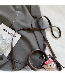 Détail du sac à main en cuir marron foncé avec bandoulière et breloque en peluche