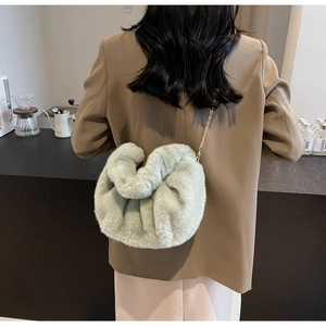 Detail of a sage green faux fur cloud bag with a delicate gold chain strap on a model