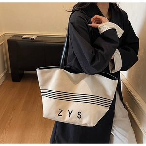 Close-up of minimalist striped canvas tote bag with black leather handles and ZYS print