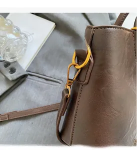 Détail d'une boucle dorée vintage et d'une bandoulière sur un sac en cuir marron foncé