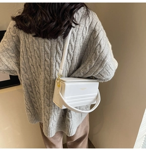 White leather shoulder bag with gold hardware worn over a grey knit sweater