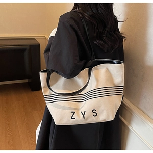 Detail of striped canvas tote bag showing black leather straps and ZYS lettering print