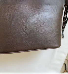 Gros plan du sac à main en cuir marron foncé avec texture grainée et logo doré embossé