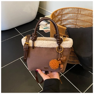 Dettaglio di finiture in pile, manico in pelle intrecciata e ciondoli su borsa in pelle