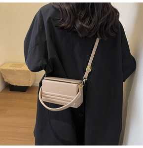 Detailed back view of a beige leather crossbody bag worn by a model in black outfit