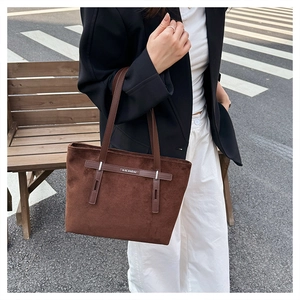 Dettaglio di una borsa tote in pelle scamosciata marrone con fibbie e tracolle lunghe