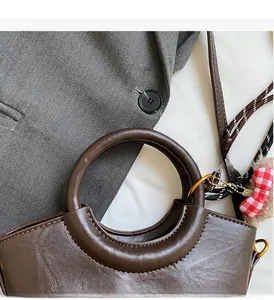 Détail d'un sac seau en cuir marron foncé avec poignée ronde et breloque en peluche