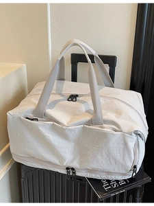 Large travel duffel bag in off-white nylon placed on a suitcase for commuting and gym