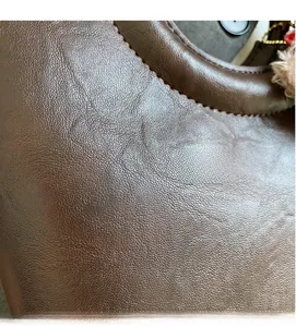 Détail en gros plan d'un sac seau en cuir marron foncé avec coutures et breloque en peluche
