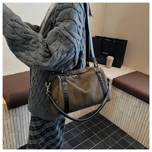 Détail du sac Boston en daim marron foncé avec poignées en cuir dans un décor d'automne