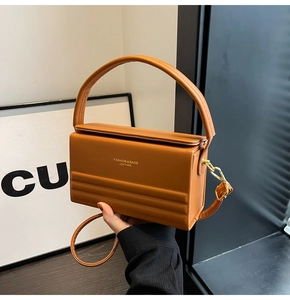 Detail of a brown leather box bag featuring gold lettering and metal strap hooks