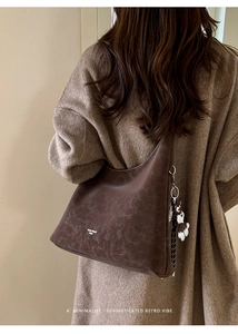 Detail of dark brown suede tote with white stitching and cute dog charm on shoulder
