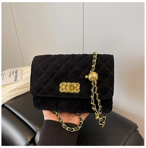 Detail of black velvet quilted crossbody bag with golden clasp and chain strap