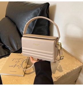 Detail of beige rectangular leather box bag with gold hardware and embossed bottom