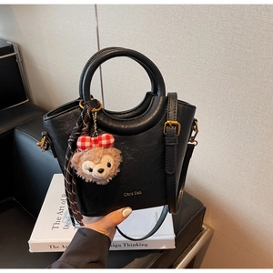 Détail du sac seau en cuir noir avec breloque en peluche et ruban à carreaux