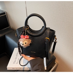Détail du sac seau en cuir noir grainé avec logo doré et charmant pendentif peluche