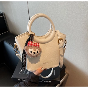 Détail d'un sac seau structuré en similicuir crème avec finitions dorées et peluche ours