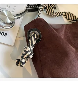 Detail of dark brown suede tote with woven rope strap and metal eyelet hardware
