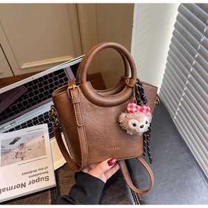 Détail d'un sac seau en cuir marron avec logo en métal et un joli pendentif en peluche