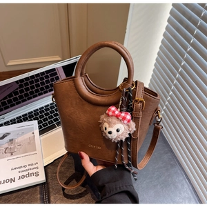 Détail d'un sac Boston en cuir marron avec poignée ronde et breloque ourson doux