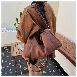 Détail d'un grand sac Boston en daim marron montrant la texture et le porté à l'épaule