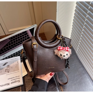 Détail du sac seau en cuir marron foncé avec boucles dorées et breloque en forme d'ours