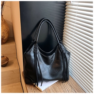 Détail d'un grand sac cabas en cuir noir avec de longues franges sur un banc en bois