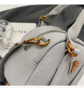 Detailed close-up of light gray pebbled leather texture and golden metal hardware on bag