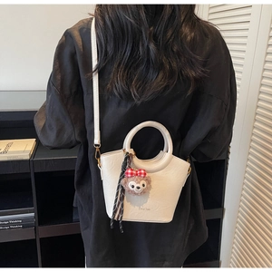 Détail du sac seau en cuir blanc avec poignée ronde et breloque peluche mignonne
