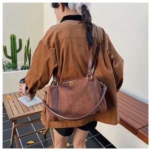 Sac Boston en daim marron porté à l'épaule dans un décor extérieur décontracté chic