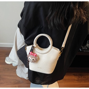 Détail du sac seau en cuir blanc texturé avec détails dorés et breloque peluche