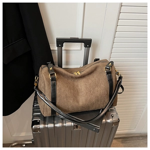 Détail d'un sac Boston en daim marron avec anses en cuir noir sur une valise argentée