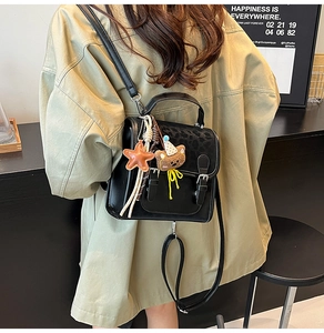 Detail of a vintage black leather backpack with a bear plush charm on a khaki trench coat