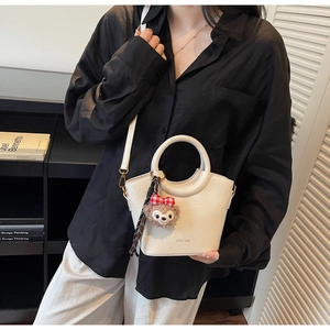 Détail du sac à main blanc texturé avec ouverture incurvée et breloque ours peluche