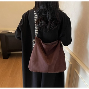 Detail of a large brown suede tote bag with a black and white striped shoulder strap