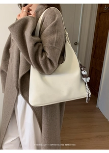 Chic cream white shoulder bag with cute bear charm shown on a brown wool coat