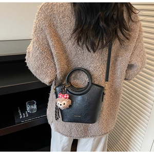 Détail du sac seau noir avec peluche et bandoulière amovible porté par le mannequin