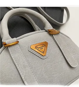 Close-up of matte grey leather bag with vintage gold triangle plaque and handle detail