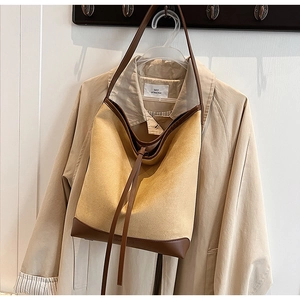 Detail of minimalist suede tote bag with brown leather trim hanging against a khaki trench coat