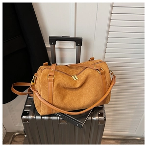 Détail du sac Boston en daim camel sur une valise argentée avec sangles en cuir brun
