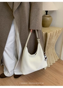 Detail of white hobo tote bag with adjustable strap and cute bear charm in cozy room