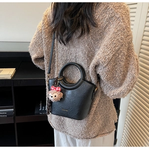 Détail d'un sac seau noir avec accessoires dorés et pendentif en peluche à carreaux