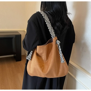 Detail of brown suede tote bag with stylish black and white striped knotted shoulder strap