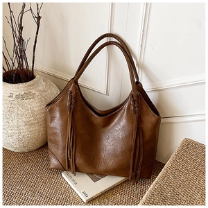 Détail d'un sac cabas en similicuir marron avec pompons et poignée tressée