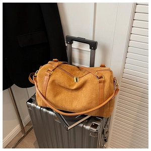 Élégant sac Boston en daim marron posé sur une valise de voyage argentée moderne.