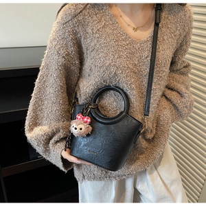 Détail du sac seau en cuir noir avec poignée ronde et breloque ours sur un pull-over