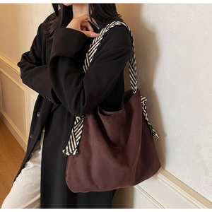 Close-up of brown suede tote bag with black and white woven strap and knot detail