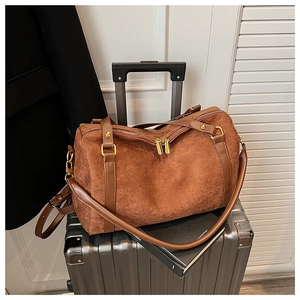 Détail d'un sac Boston en daim marron avec anses en cuir posé sur une valise argentée