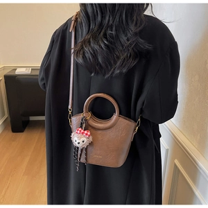 Détail du sac seau en cuir marron foncé avec poignée et accessoire de charme d'ours