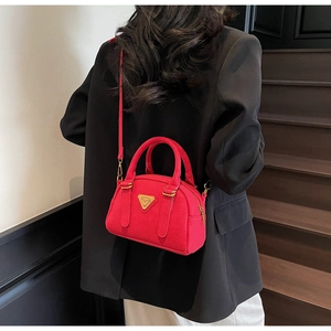 Close-up of red leather Boston bag with gold triangle logo and crossbody strap details